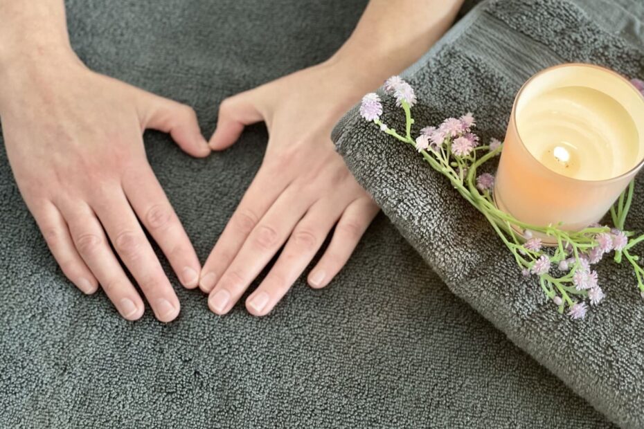 Nina's hands shaped into a love heart on folded grey towels next to some lavender with a candle scented burning.